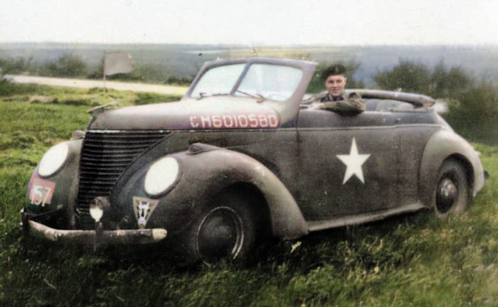 Le Capitaine Duncan avec sa nouvellement capturée (et repeinte) voiture d’état-major quelque part dans la brèche de Falaise en août 1944. La voiture, une Matford (Ford) française de 1933, fut plus tard surnommée « the passion wagon ».